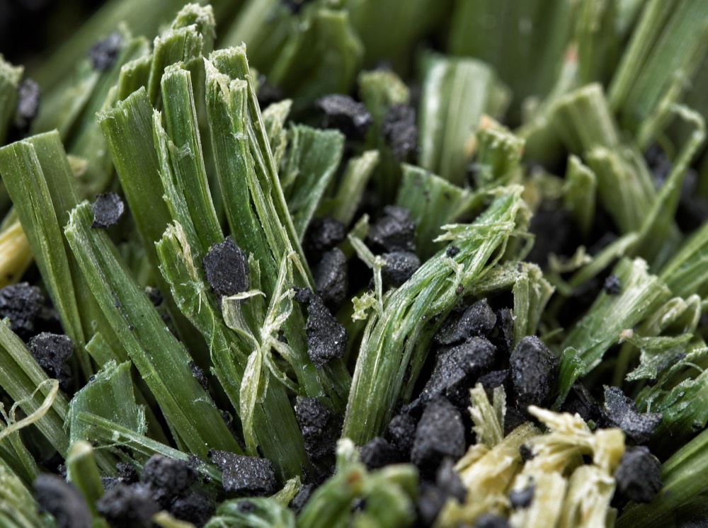 Macro photograph of worn, frayed artificial grass fibres with loose rubber crumb