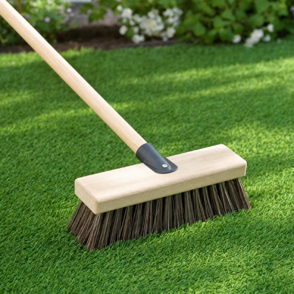 Stiff-bristled yard brush lying on artificial grass